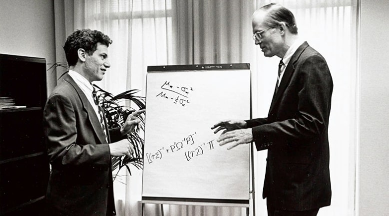 A black-and-white photo of Robert Litterman and Fischer Black chatting in an office in 1994